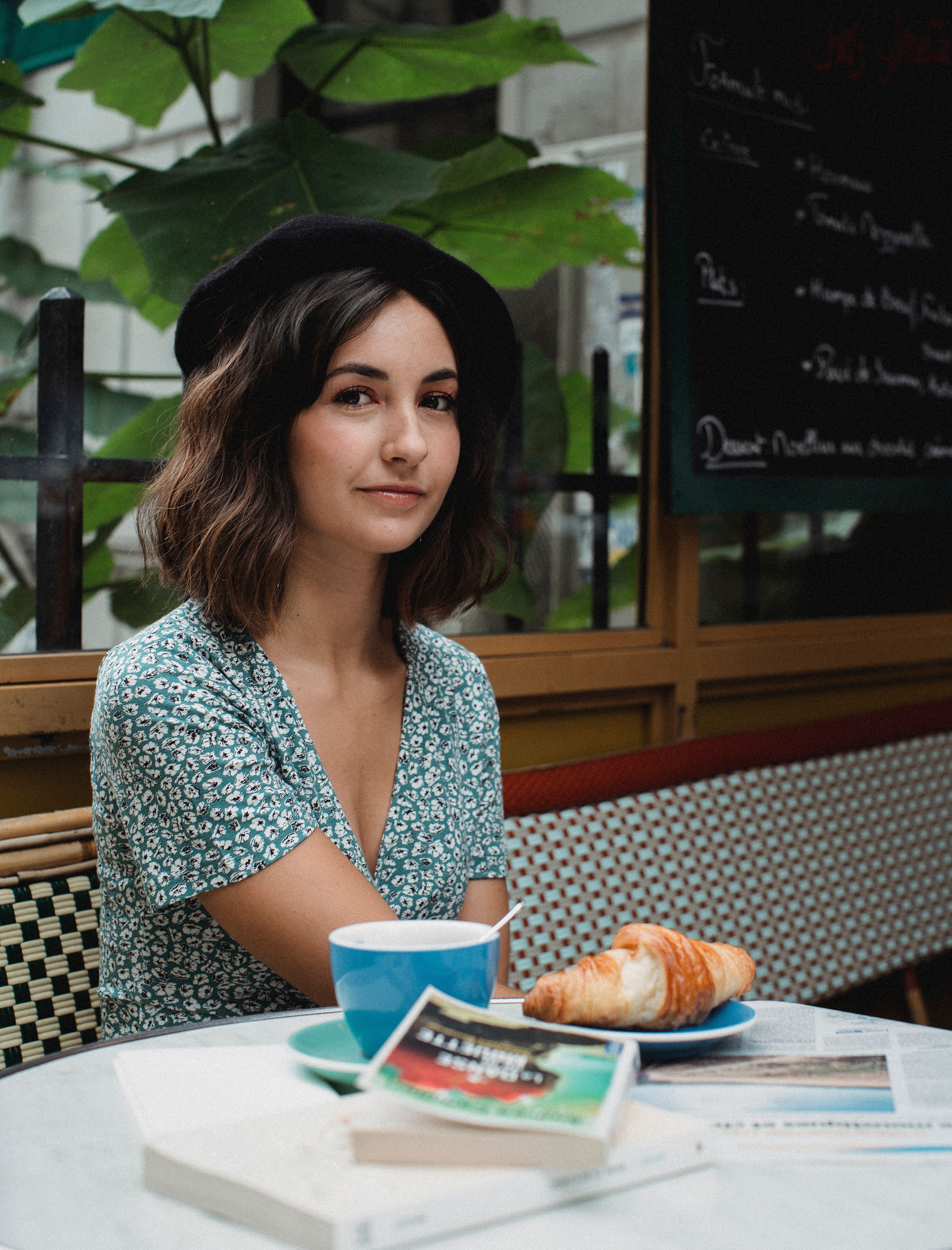 Young woman with coffee and croissant at a café, exuding a relaxed and casual vibe.