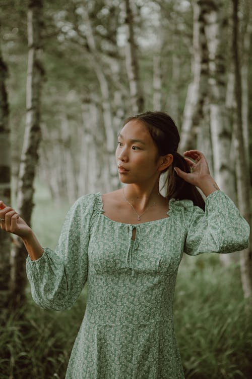 Pensive ethnic woman touching hair while having relaxation in forest