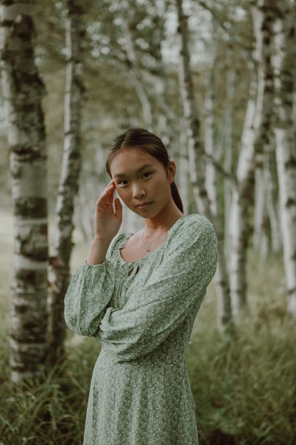 A serene portrait of a woman in a green dress standing among birch trees.