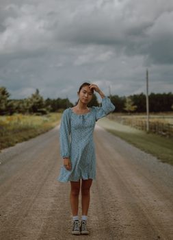 一名穿着夏装的亚洲女性，正站在农村空荡荡的道路上，陷入深思