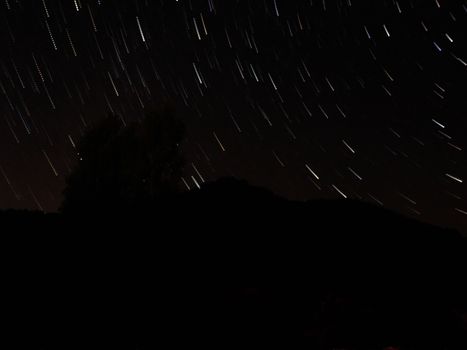 Star trails creating a dynamic pattern in the night sky over a dark mountainous silhouette.