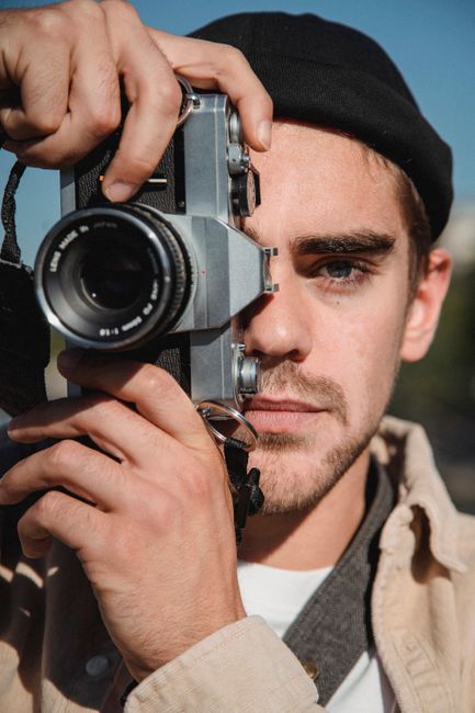 Portrait of a young man using a vintage camera outdoors in a city.