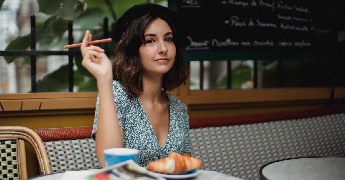 young woman sitting at outdoor cafe in European village with journal and coffee