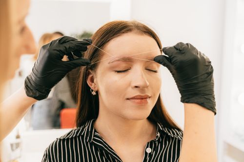 Free A woman receives precise eyebrow threading in a modern salon setting. Stock Photo