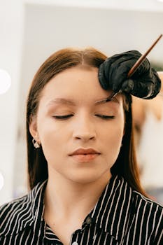A woman undergoing precise eyebrow microblading treatment indoors.