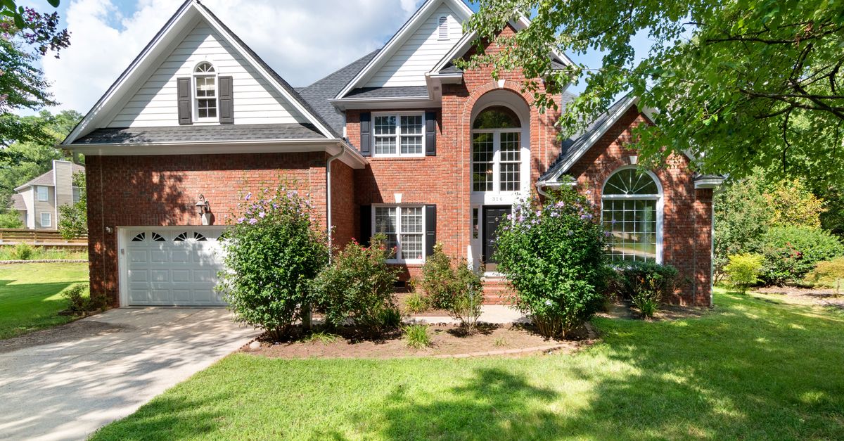 Charming two-story brick house in sunny suburb with lush front lawn.