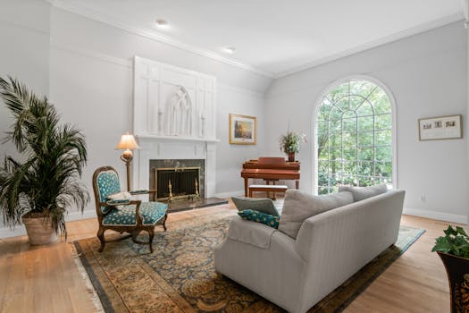 Bright living room featuring a piano, fireplace, and large arched window.