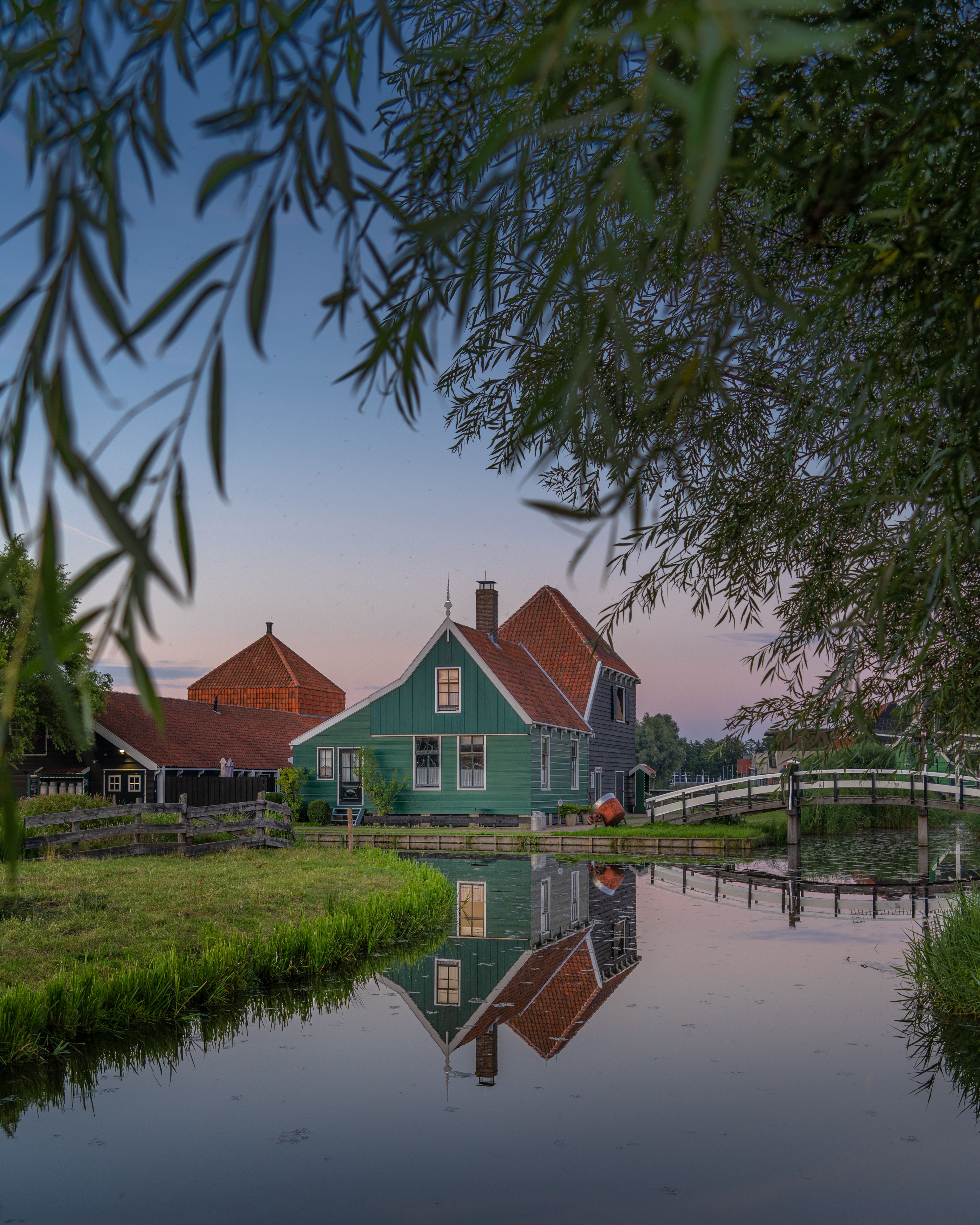 A traditional house sitting directly beside a bridge over water, reflected in the calm water below
