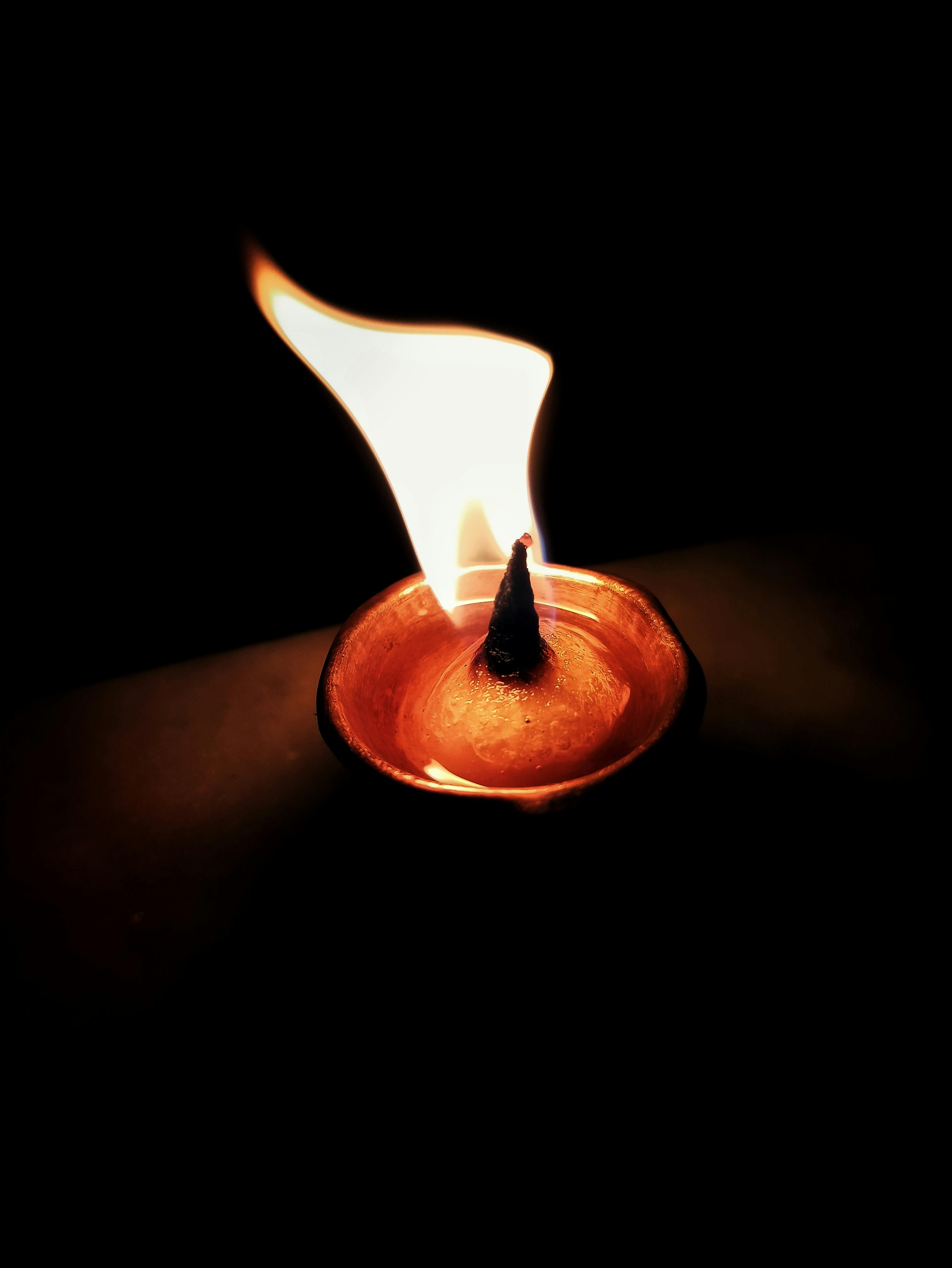 Close-up of a traditional Indian oil lamp with a warm flickering flame in a dark setting.