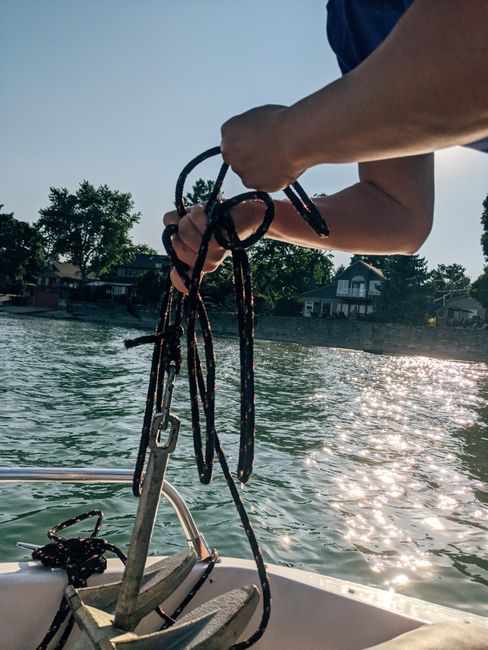 Crop unrecognizable person holding rope with anchor on yacht in sea water near coast