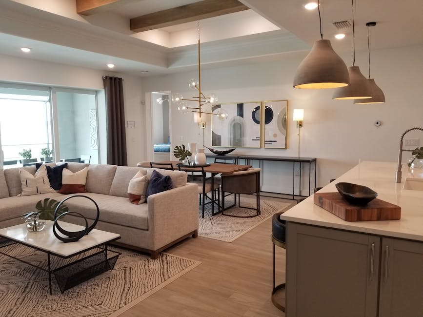 home staging - how to sell my house fast for cash portland Modern staged living room with a sectional sofa, decorative pillows, and a coffee table, featuring a dining area with a stylish light fixture, showcasing an inviting atmosphere ideal for attracting potential buyers in Portland.