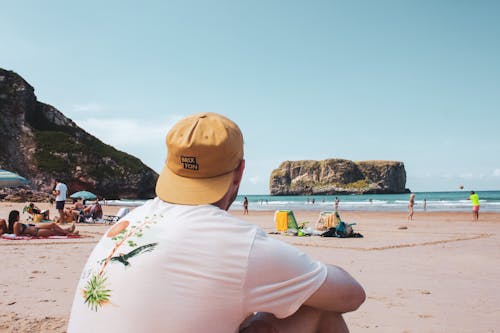 Free Person Wearing a Yellow Cap and White Shirt Sitting on Sand Stock Photo