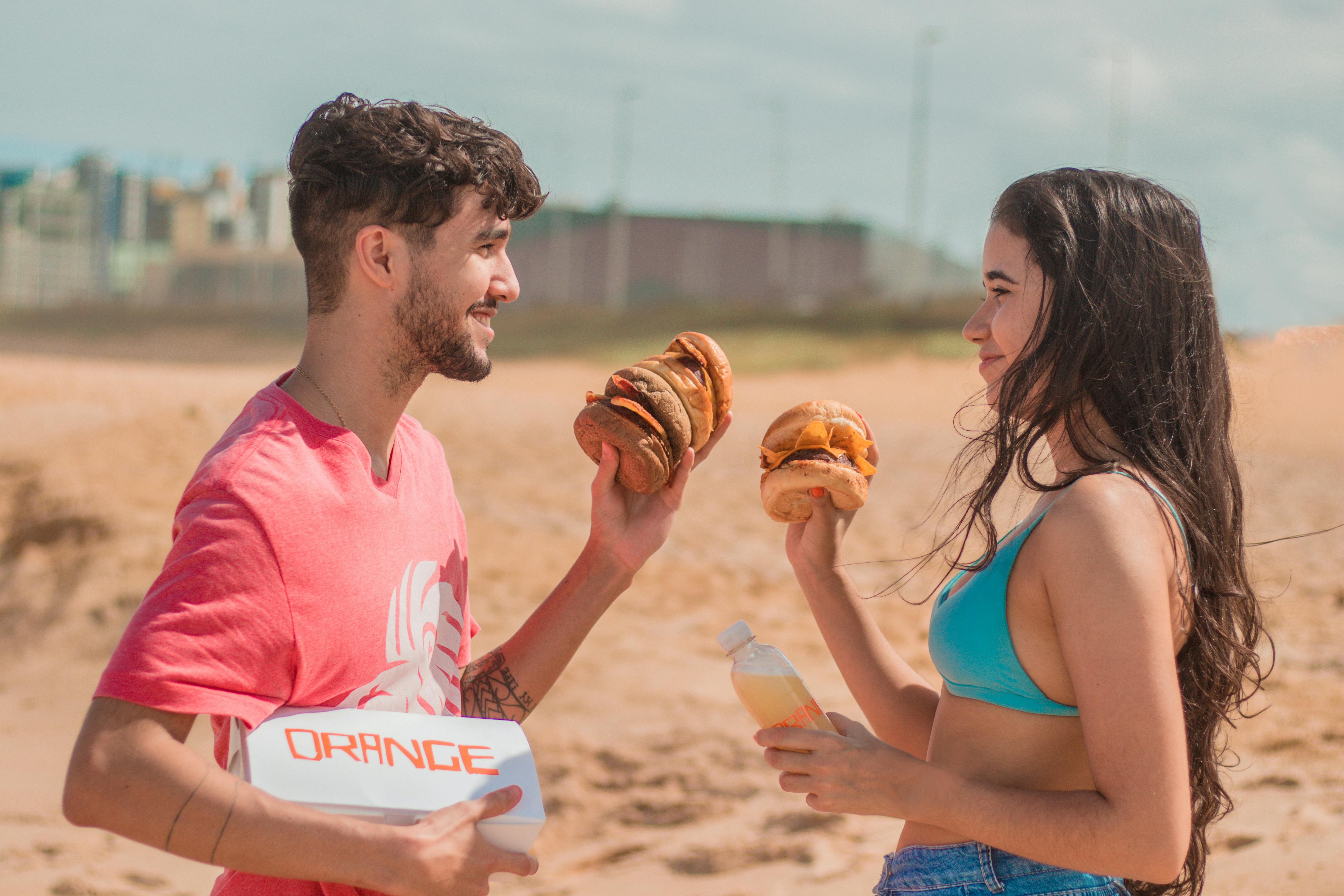 Two adults enjoying burgers on a sunny beach, embodying summer fun and leisure.