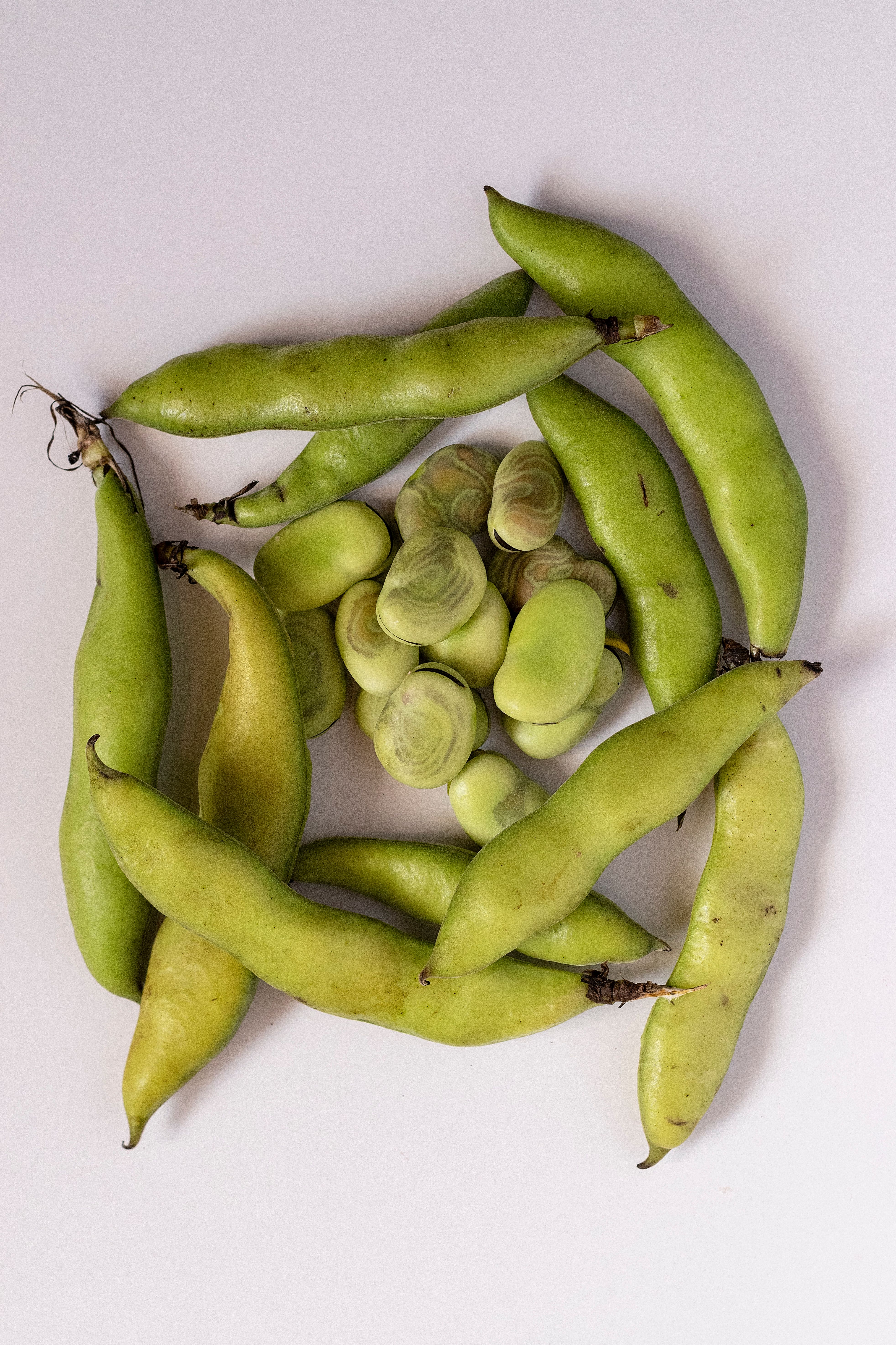 A high-angle view of fresh fava beans and pods creatively arranged on a white background.
