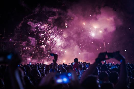 Back view of anonymous crowd of people recording video of performance on cellphones in concert hall with shiny spotlights illuminating scene