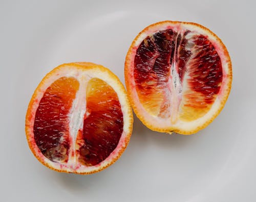 Top view of halves of juicy tasty sliced healthy red orange placed on white background