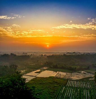 Peaceful aerial view of sunrise over lush farmland in Rumpin, West Java, Indonesia.