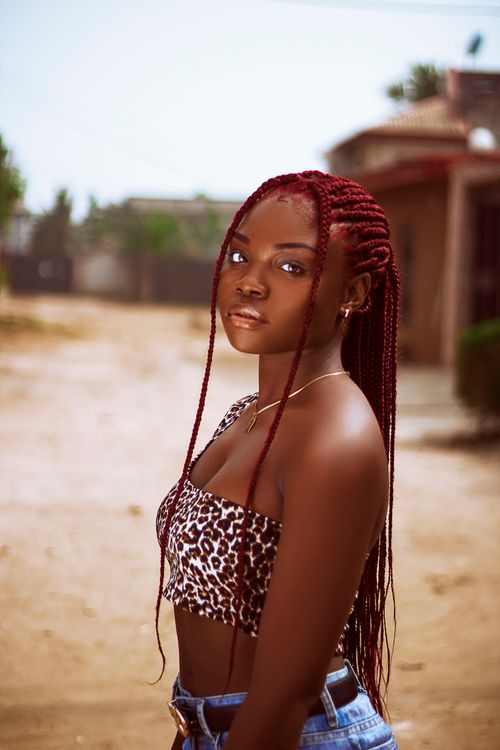 Free Serious young black female with long red African braids in stylish top standing on sandy road in sunny day Stock Photo