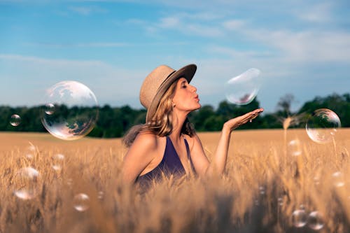 Woman in Brown Sun Hat and Sitting on Brown Grass Field