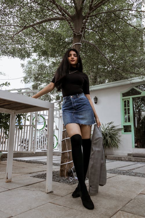 Woman in Black Shirt and Blue Denim Skirt Leaning on a Table