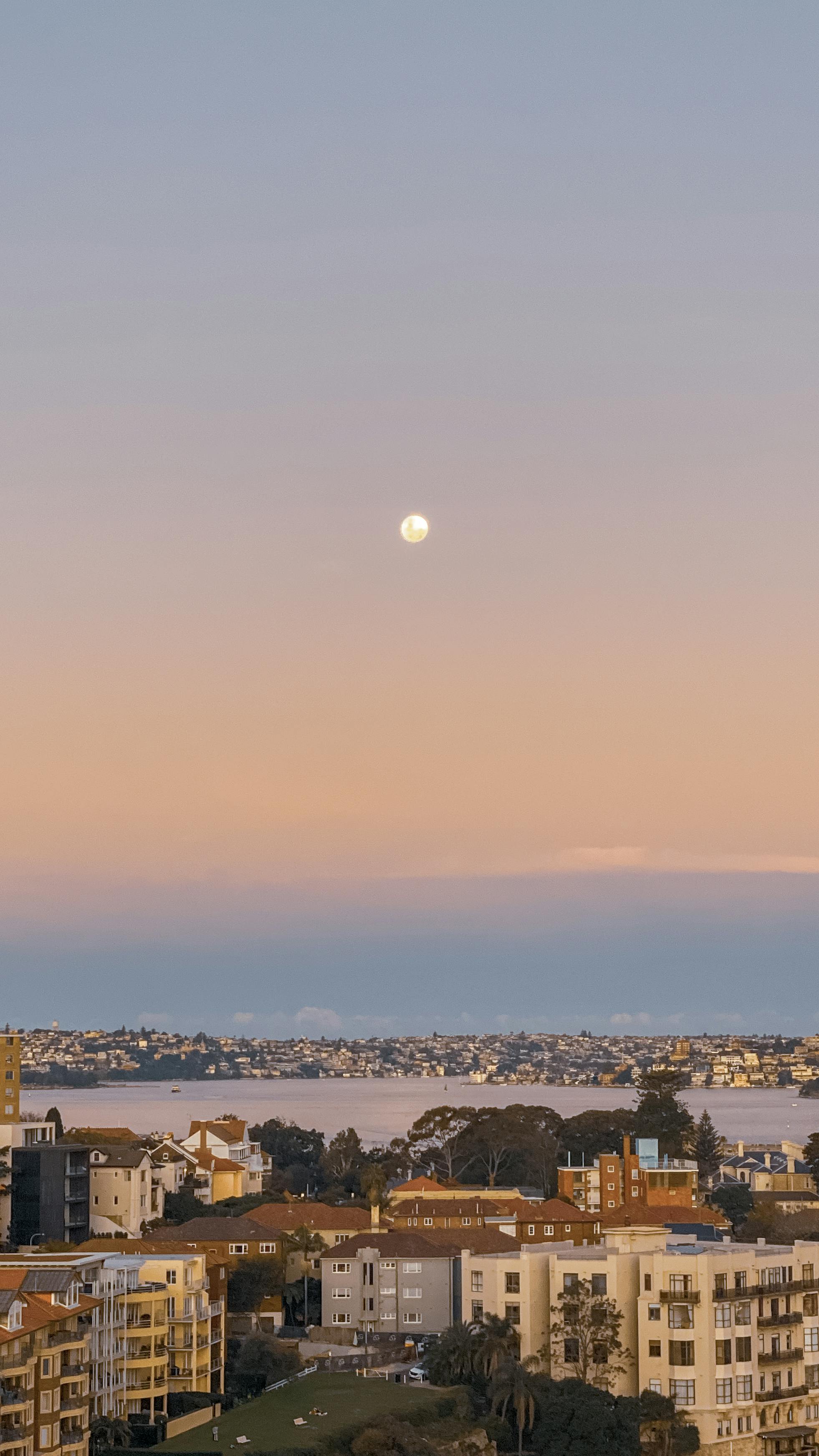 Breathtaking aerial view of Sydney cityscape at dusk with a full moon and colorful sky.