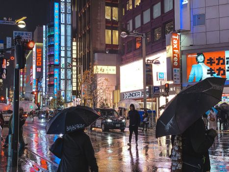 雨夜的东京街头，霓虹灯光映照在潮湿的人行道上，充满活力
