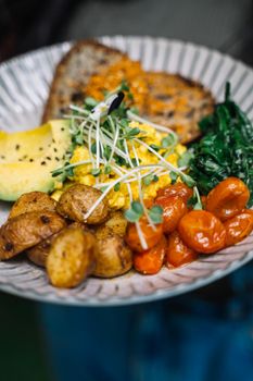 Colorful breakfast with eggs, potatoes, tomatoes, spinach, and toast on a plate.