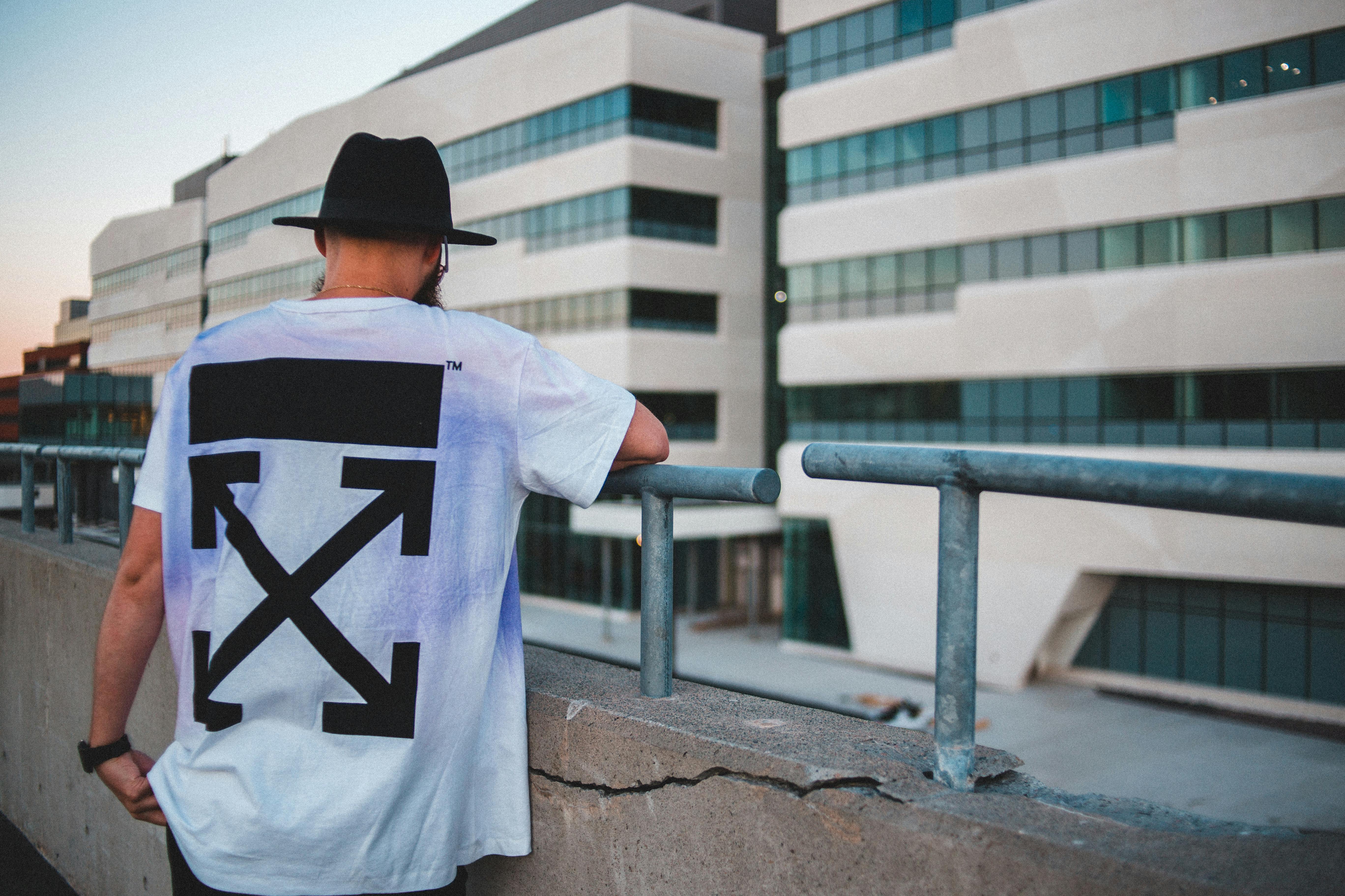 Back view of anonymous male in hat and trendy T shirt resting near shabby railing