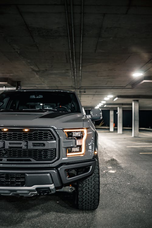 Modern gray pickup truck with bumper and illuminated headlights lamps placed on empty parking lot with columns  in evening time