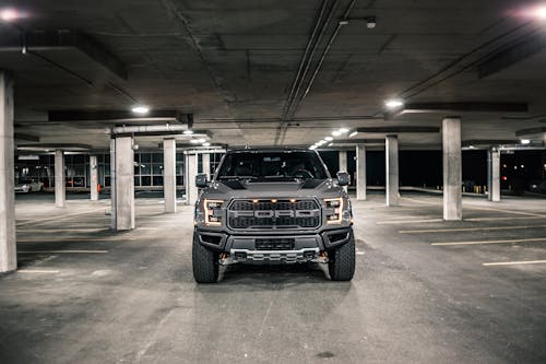 Modern gray pickup with glowing headlights parked on asphalt in underground parking lot with columns in evening time in city