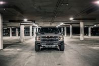 Modern gray pickup with glowing headlights parked on asphalt in underground parking lot with columns in evening time in city