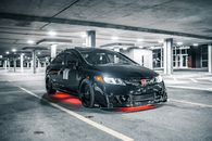 Modern black automobile with glowing headlights and illumination in underground parking lot with marking lines and columns in evening time