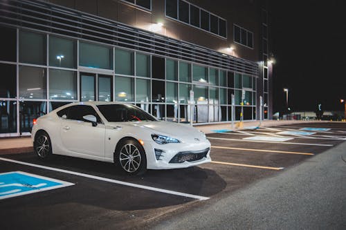 Expensive white automobile on parking space with marking lines near building with glass wall in street at night time