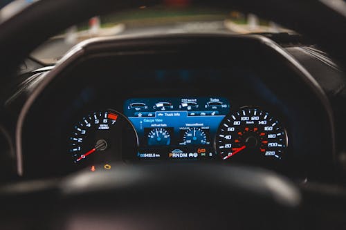 View of glowing instrument panel through steering wheel of contemporary automobile with black interior and blurred street through windshield outside