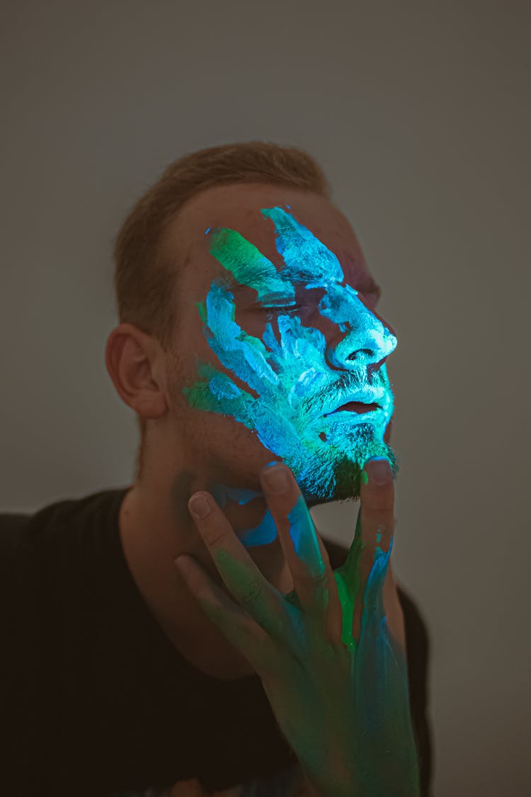 Calm Man With Neon Paint On Face Touching Chin