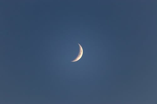 Bright narrow white crescent in blue peaceful sky in late dusky calm evening