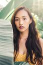 一名年轻女子身穿黄色圆点连衣裙，站在大片绿叶中，阳光洒落在她身上