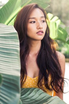 阳光明媚的热带花园里，绿树成荫，一名年轻女子若有所思地站在那里