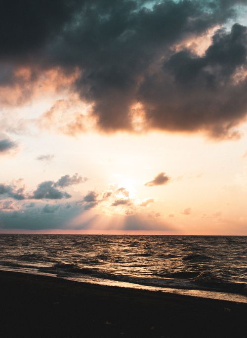 Free Captivating ocean scene at sunset with dramatic clouds casting rays over the horizon. Stock Photo