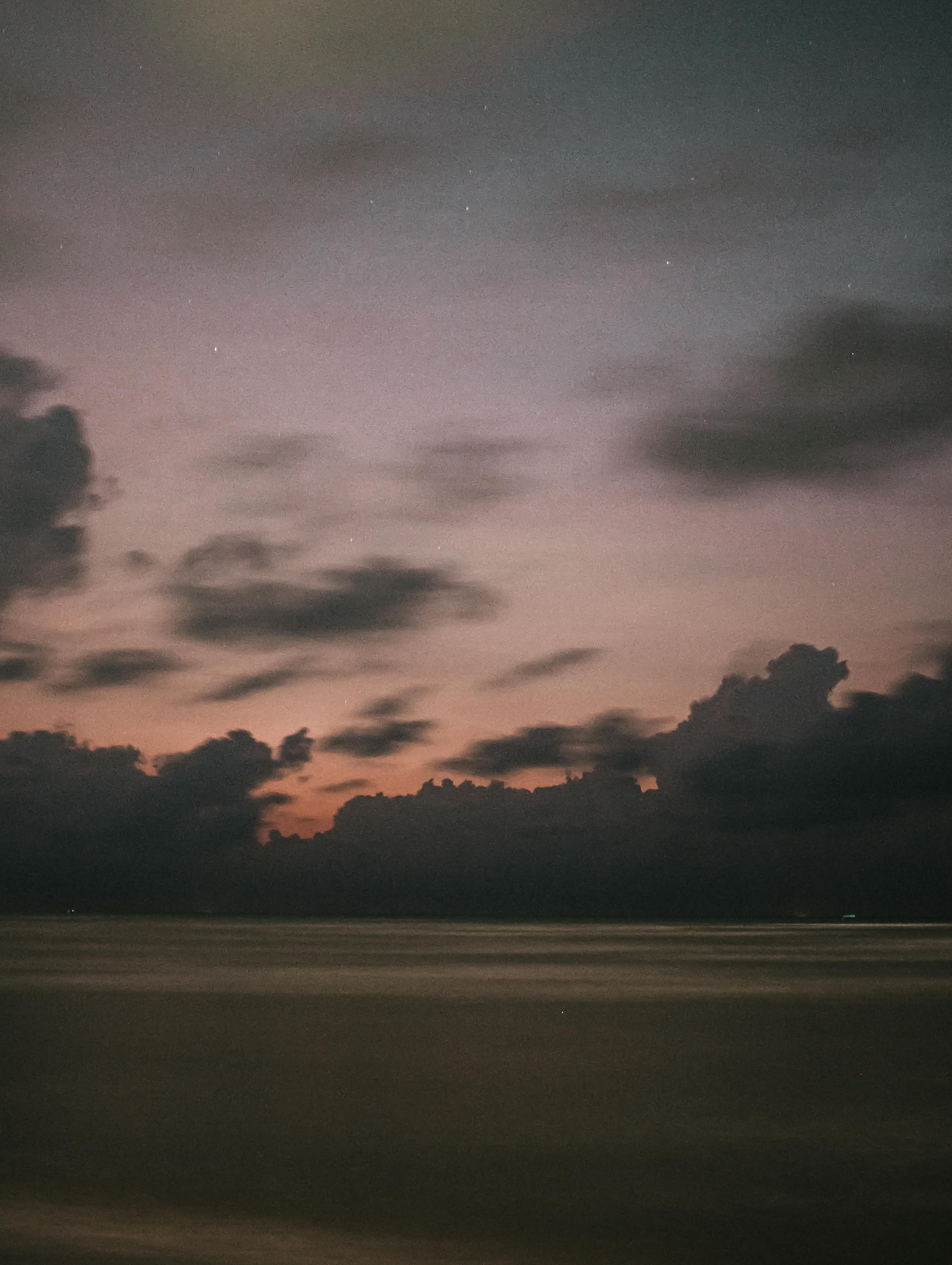 Serene beachscape with dramatic clouds and twilight hues, perfect for mobile wallpaper.