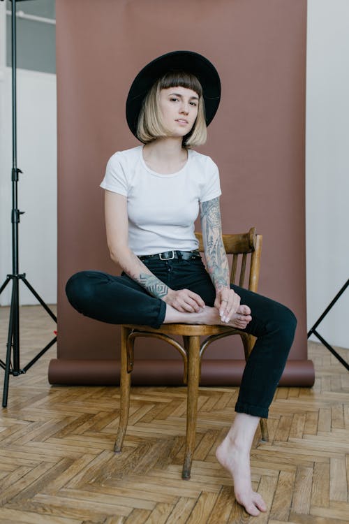 Woman in White Crew Neck T-shirt Sitting on Brown Wooden Chair