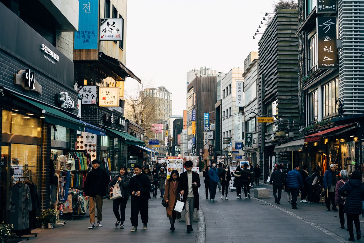 A busy shopping street in Seoul with people walking past shops