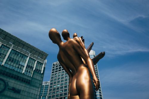 Free A striking bronze sculpture set against a modern city skyline under a clear blue sky. Stock Photo