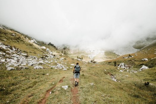 一名孤独的徒步旅行者，在瑞士阿尔卑斯山迷雾重重的小径上探索，周围是岩石地形和郁郁葱葱的绿色植物