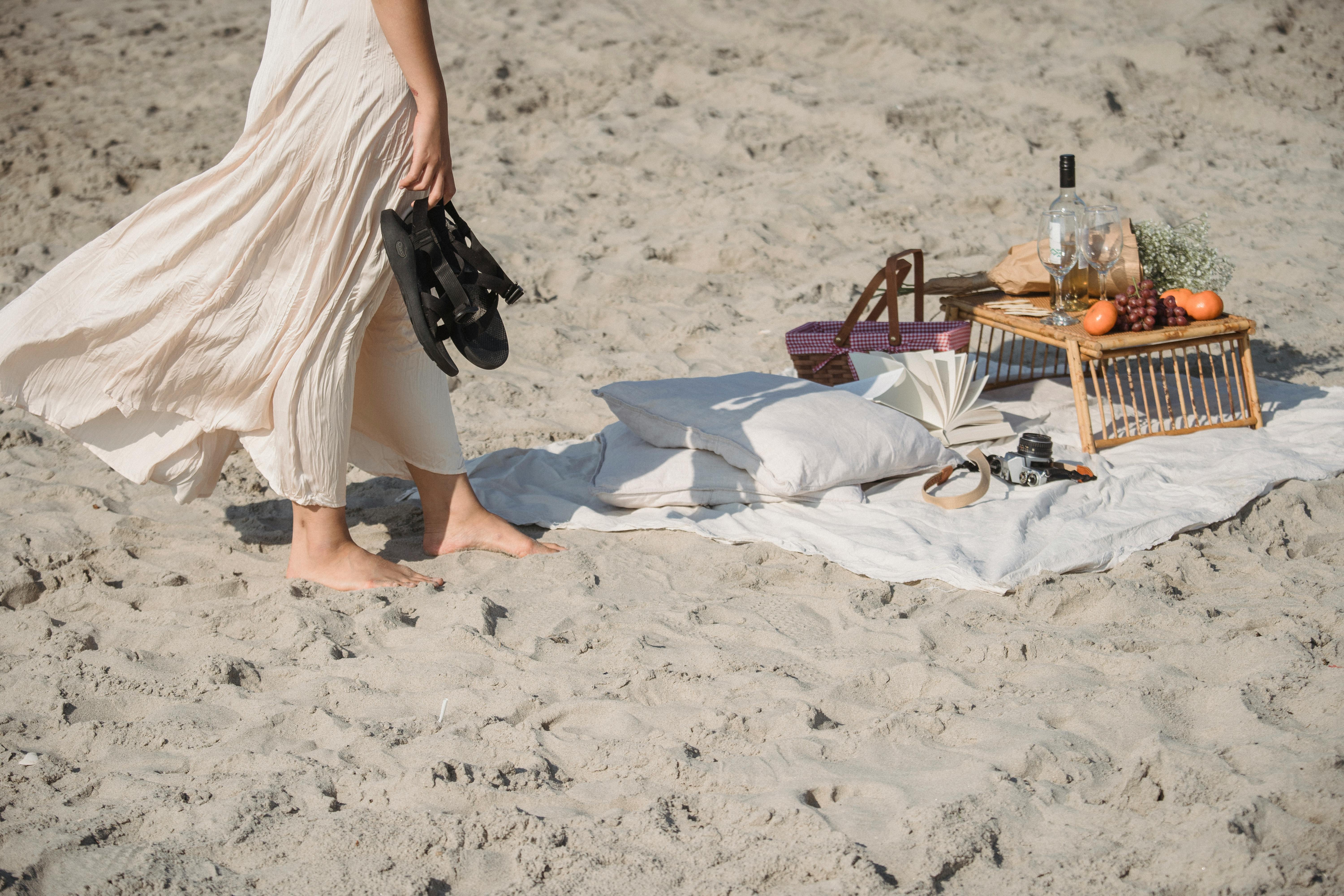 Una tranquila configuración de picnic en la playa con una persona disfrutando de un paseo descalzo junto a la orilla.