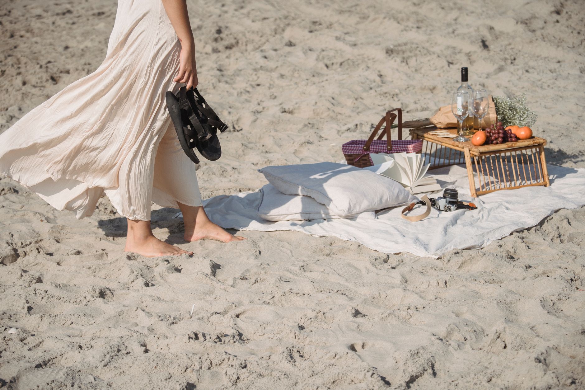 Una tranquila configuración de picnic en la playa con una persona disfrutando de un paseo descalzo junto a la orilla.
