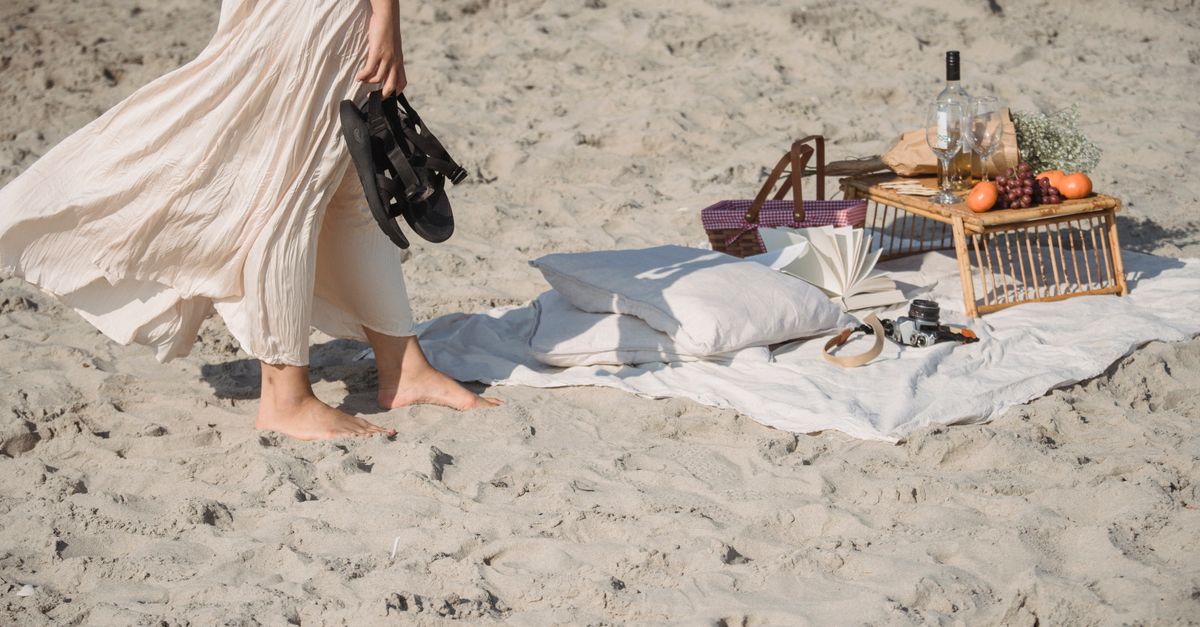 A tranquil beach picnic setup with a person enjoying a barefoot stroll by the shore.
