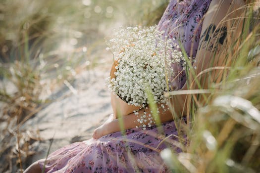 A woman in a floral dress sits outdoors holding a bouquet of Gypsophila flowers, surrounded by grass.