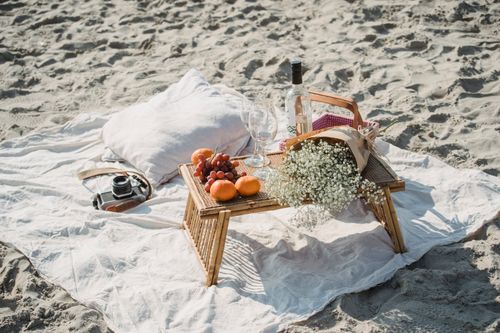 Free Enjoy a serene beach picnic with fruits, flowers, wine, and a vintage camera arrangement. Stock Photo