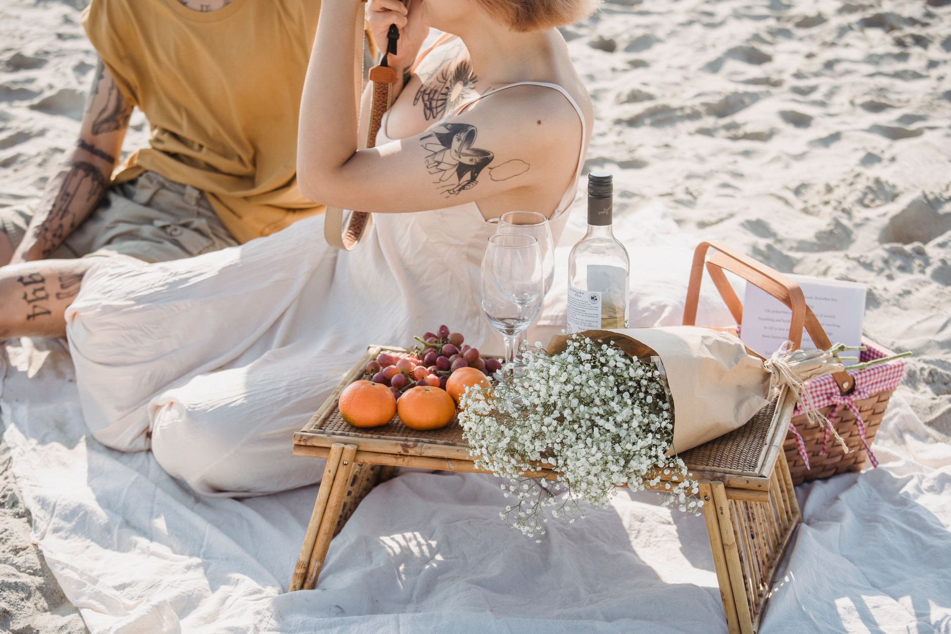 Una acogedora escena de picnic en la playa con vino, frutas y flores, perfecta para una reunión de pareja.